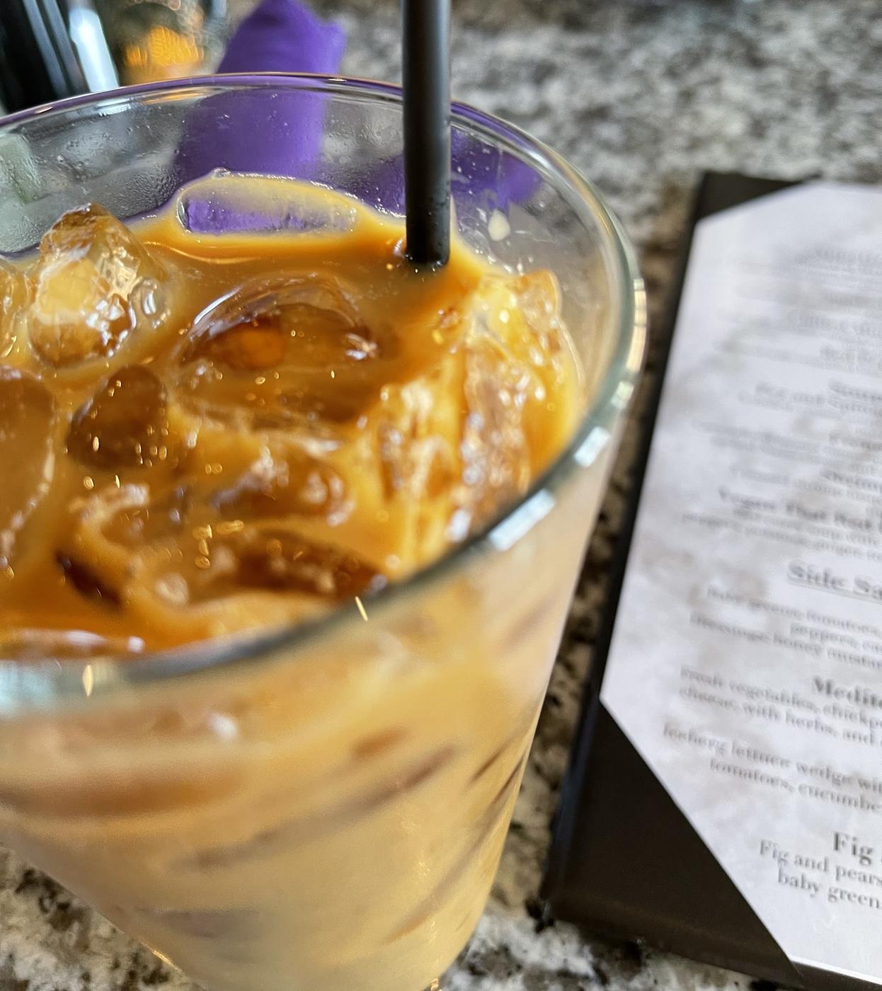 An iced coffee in a tall glass on a speckled stone table, beside a folded purple napkin.